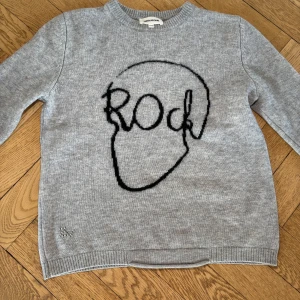 Grå tröja med tryck från Zadig & Voltaire - Snygg grå tröja från Zadig & Voltaire med ett coolt svart 'Rock'-tryck i form av en skalle på framsidan. Tröjan har långa ärmar och är perfekt för en avslappnad stil. Passar bra till jeans eller kjol för en trendig look. Tröjan är i nyskick och mycket varsamt andvänd❤️ om du vill mötas upp och hämta tröjan görs det på Karlaplan 