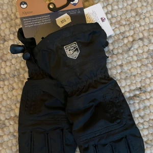 Svarta skidhandskar från Hestra strl 6 NYA - Säljer ett par svarta Hestra skidhandskar, strl 6, perfekta för alpina aktiviteter. De har justerbara remmar och är designade för att hålla händerna varma under kalla vinterdagar. Helt nya med tag kvar. Aldrig använda. hämtas Södermalm, Mosebacke Slussen, Medborgarplatsen