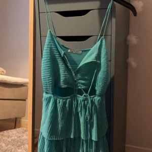 Turkos klänning från Zara - Snygg turkos klänning från Zara med smala axelband och volangdetaljer. Klänningen har en omlott-design och är perfekt för sommarens alla tillfällen. Tillverkad i ett lätt och luftigt material.