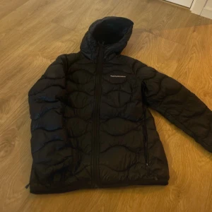 Svart pufferjacka från Peak Performance - Säljer en svart pufferjacka från Peak Performance. Jackan har en dragkedja framtill och är perfekt för kyligare väder. Den är stilren och funktionell med långärmade ärmar och en bekväm passform. Knappt använd! 