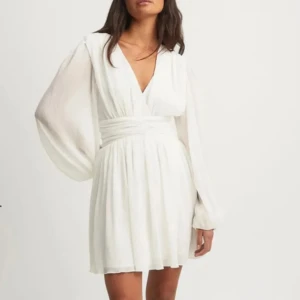 Studentklänning  - Köpt på NAKD! Elegant vit kortklänning med v-ringning och långa, flödande ärmar. Perfekt till studenten. Har använt den en gång och därav väldigt fint skick! Nypris 649kr.