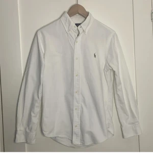 Vit Ralph lauren skjorta  - Klassisk vit skjorta från Ralph Lauren med broderad logotyp på bröstet. Skjortan har långa ärmar och knappar framtill. Perfekt för en stilren look.