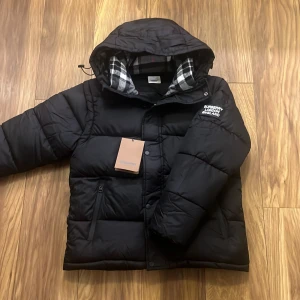 Svart dunjacka/väst från burberry - Snygg svart dunjacka från Burberry med huva och dragkedja. Går även att göra till väst. Helt ny.