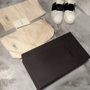 Valentino Open skor - Snygga Valentino Open sneakers i vitt med en bred svart rem över snörningen. Skorna har en stilren design med vita sulor och diskreta detaljer. Perfekta för en trendig look. Ny pris 6000 jag säljer för 3799 kan gå ner i pris vid snabb affär 😊kvitto finns. Skcik 9/10