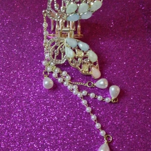 Hårklämma med pärlor och vita stenar - Elegant hårklämma i guld med vita stenar och hängande pärlor. Perfekt för att ge en glamorös touch till din frisyr.