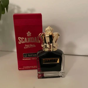 Scandal Le Parfum av Jean Paul Gaultier - Elegant och djärv parfym från Jean Paul Gaultier. Flaskan har en unik design med en gyllene krona som lock och en djup svart färg. Förpackningen är röd med guldtext. Perfekt för den som vill sticka ut med en lyxig doft. 40/ml av en 50 ml flaska kvar. 