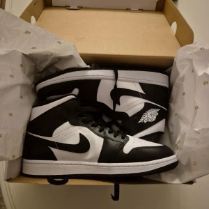 Svartvita Nike Air Jordans - Snygga svartvita Nike Air Jordans med klassisk design. Skorna har en hög siluett med snörning och den ikoniska Air Jordan-loggan på sidan. Perfekta för dig som vill ha en stilren och sportig look. Oanvända 