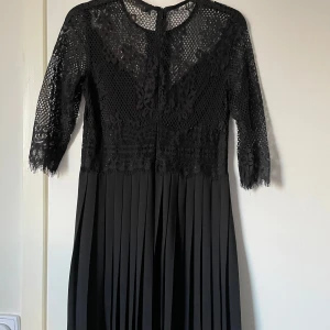 Svart spetsklänning från Zara  - Elegant svart klänning från Zara Basic med spetsdetaljer och trekvartsärmar. Klänningen har en vacker plisserad kjol och en dragkedja i ryggen. Perfekt för en stilfull kväll.