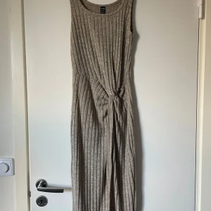 Beige ribbad klänning - Snygg beige ribbad klänning med knytning i midjan. Den är ärmlös och har en lång design som ger en elegant look. Perfekt för både avslappnade och mer uppklädda tillfällen.
