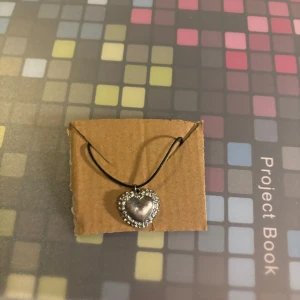 Halsband med hjärtberlock - Charmigt halsband med en hjärtformad berlock i silverfärg, omgiven av glittrande stenar. Perfekt för att ge en extra touch av elegans till din outfit.