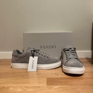 Grå sneakers från Sandö - Snygga grå sneakers från Sandö i mocka med vit sula. Levereras i originalkartong. Helt nya ändast testade inomhus✅
