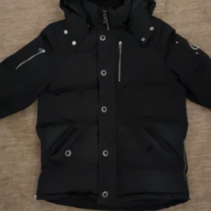 Moose Knuckles Q3 - Svart dunjacka från Moose Knuckles med dragkedja och knappar framtill. Jackan är i storlek M och säljes billigt pga att för det första har en knapp lossnat och för det andra har jag tappat bort pälsen. Kvitto finns och vid frågor eller funderingar är det bara att skriva.