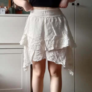 Vit volangkjol - Supersöt och charmig vit kjol med flera lager av volanger och broderade detaljer. Asymmetrisk och unik design som jag tycker bidrar till kjolens sagolika känsla. Alldeles för liten på mig tyvärr, står storlek 40 men skulle säga att den är liten i storlek. Dragkjedja i sidan🩷