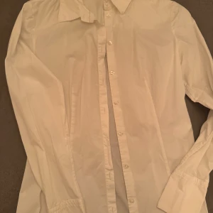 Vit skjorta från Hugo  - Klassisk vit skjorta från Hugo i bomulls stretch, storlek 36. Skjortan har långa ärmar och knappar framtill. Perfekt för en stilren look.