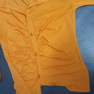Orange blus med knappar - Snygg orange blus med knappar framtill och rynkade detaljer. Perfekt för att liva upp garderoben med en färgklick.bra skick andvänd 1 gång 