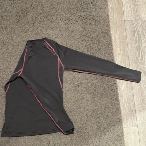 Svart kompressionströja från OTP - Säljer en svart kompressionströja från OTP med rosa sömmar. Tröjan har långa ärmar och är perfekt för träning. Materialet är syntetiskt och designat för att ge stöd och komfort under aktivitet, andas väldigt bra och tar in svett.