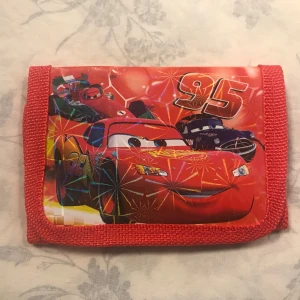 Cars Barn Plånbok  - Två färgglada plånböcker med motiv av Blixten McQueen från filmen Bilar. Den ena plånboken är röd med nummer 95 och den andra är blå med flerfärgade detaljer och racingtema. Helt ny , 55kr/st , sammafrakt 