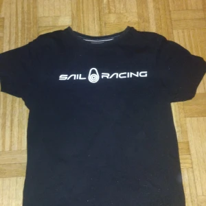 Svart t-shirt från Sail Racing - Snygg svart t-shirt från Sail Racing med vit logga på bröstet och nacken. Perfekt för en casual look. Tillverkad i mjukt material för bekväm passform.