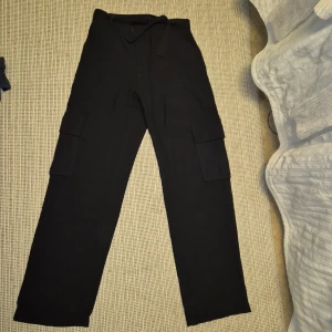 Svarta cargobyxor från Lindex - Snygga svarta cargobyxor från Lindex med praktiska fickor på sidorna. Perfekta för en avslappnad och trendig look. Tillverkade i ett bekvämt material som passar till många olika stilar.