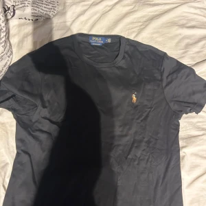 Svart t-shirt från Polo Ralph Lauren - Snygg svart t-shirt från Polo Ralph Lauren med det klassiska broderade logotypen på bröstet. T-shirten har en normal passform och är tillverkad i bomull för en bekväm känsla. Skick 10/10 säljer den på grund av att den aldrig använda pris kan diskuteras vid en snabb affär 