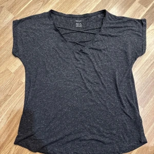 Grå t-shirt  - En mörkgrå t-shirt från Esmara i storlek M med en snygg korsad detalj vid halsringningen. T-shirten har korta ärmar och en avslappnad passform!