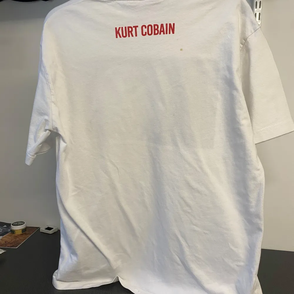 Snygg vit t-shirt från Zara med ett stort tryck av Kurt Cobain på framsidan och hans namn i rött på baksidan. Citatet 'I can't sing or play or rhyme, I think that's just fine' finns under bilden. Perfekt för fans av rockikoner! Tror storleken är fel markerad eftersom den är väldigt stor. Kan vara storlek M. T-paidat.