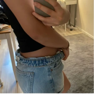 Blå jeansshorts - Säljer ett par blå jeansshorts med en avslappnad passform. Shortsen har en klassisk femficksdesign och är perfekt för sommardagar. De är lågmidjade och har en lätt tvättad look.