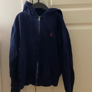 Blå ralph lauren zip hoodie  - Marinblå/navyblå hoodie med dragkedja i märket Ralph lauren. Använd ca 5 ggr (tror jag😅??) och har inga skador eller märken att den är använd bara att den är lite torr i tyget bara. Det har tyvärr blivit för liten