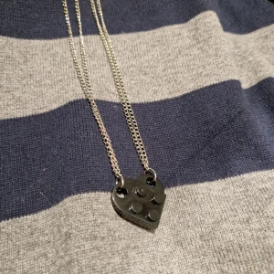 Halsband med hjärtformade hängen - Två halsband med varsinn legobit som tillsammans formar ett hjärta. Kedjorna är tunna och silverfärgade. 