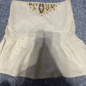Beige kjol med pärldetaljer - Snygg beige topp med volang och dekorativa pärlor i ett mönster framtill. Toppen har en elastisk del baktill för bättre passform. Står L på lappen men den passar S-L pga de elastiska där bak.🥯🧮