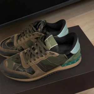Valentino Rockrunner i camouflage - Snygga Valentino Rockrunner sneakers i ett coolt camouflage-mönster. Skorna har en mix av gröna och bruna nyanser med svarta detaljer och en ljusblå häl. Perfekta för en trendig look. Riktigt feta valentinos på marknaden🙌