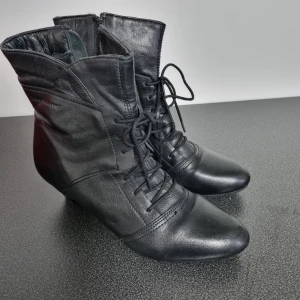 Svarta boots från Ten Points - Snygga svarta boots i skinn från Ten Points med snörning och dragkedja. De har en spetsig tå och en diskret klack, vilket ger en elegant look. Perfekta för både vardag och mer uppklädda tillfällen.