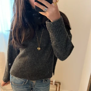 Mörkgrå stickad tröja - Säljer en mysig mörkgrå stickad tröja med långa ärmar och ribbade detaljer vid ärmslut och nederkant. Perfekt för kyliga dagar och enkel att matcha med olika outfits. 