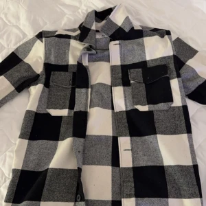 Svartvit rutig overskjorta - Snygg svartvit rutig overshirt med långa ärmar och knappar framtill. Perfekt för lager-på-lager-stil och har två praktiska bröstfickor. En klassisk och tidlös design som funkar till många tillfällen. Storlek S, från cubus.