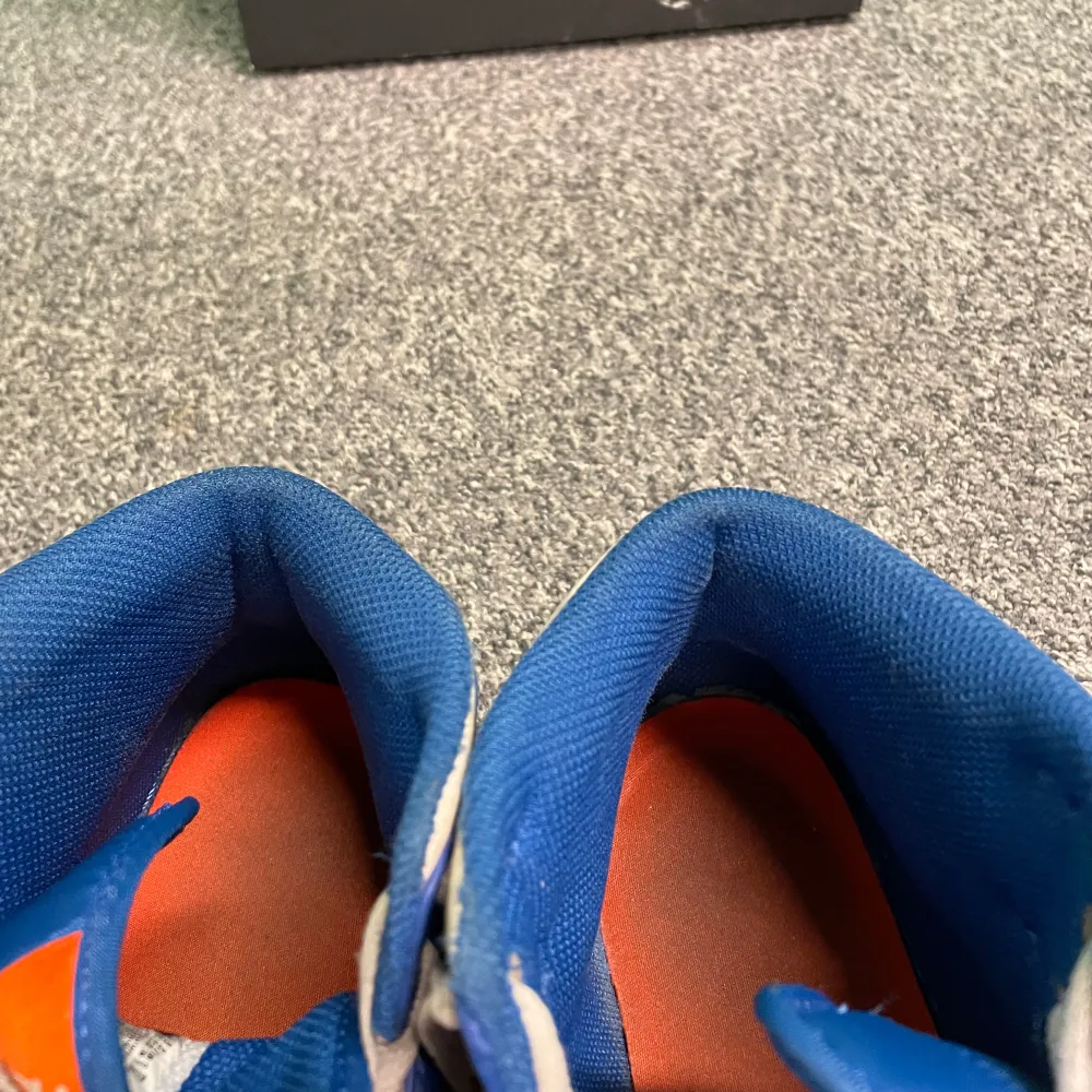Snygga Nike Air Jordans i en fräsch kombination av blått, orange och vitt. Skorna har klassisk snörning och en iögonfallande orange sula. Perfekta för dig som vill sticka ut med stil.. Kengät.