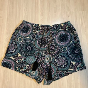 Mönstrade shorts med knytband - Snygga shorts med ett färgglatt mönster i blått, rosa och grönt. De har ett knytband med tofsar i midjan för en justerbar passform. Perfekta för en avslappnad sommarlook.