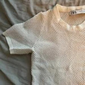 Vit kortärmad tröja från Zara - Säljer en stilren vit tröja från Zara med korta ärmar och ett unikt texturerat mönster. Perfekt för en avslappnad look. Tröjan är i storlek M och har en bekväm passform.