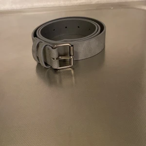 Grått bälte med silverfärgat spänne - Snyggt grått bälte med ett stilrent silverfärgat spänne. Perfekt för att ge en modern touch till din outfit. Bältet har en klassisk design och passar till många olika stilar.