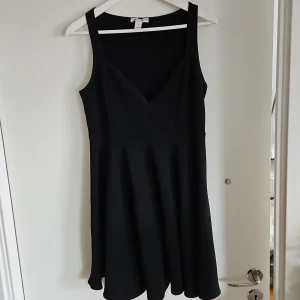 Svart klänning - Snygg svart klänning med v-ringning. Perfekt för en stilren look. Klänningen har en elegant passform och är lätt att matcha med olika accessoarer.