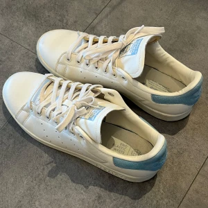 Vita Adidas Stan Smith sneakers med ljusblå detaljer - Säljer mina Stan Smiths som inte passade mig. Mycket bra skick, se bilder. Använda ett fåtal gånger. 