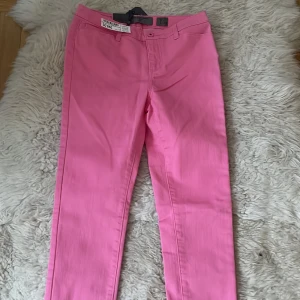 Rosa byxor från Vero Moda 27/34 nya - Snygga rosa byxor från Vero Moda med en tight passform. Byxorna har en klassisk design med knappar och dragkedja framtill. Perfekta för att lägga till en färgklick i garderoben.