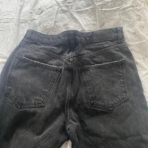 Svarta jeans med slitningar - Säljer ett par svarta jeans med coola slitningar på benen. De har en klassisk femficksdesign och knappgylf. Perfekta för en avslappnad stil.