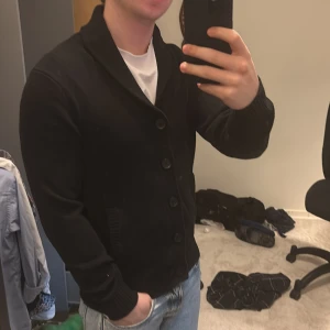 Svart kofta med knappar - Säljer en stilren svart kofta med knappar framtill. Den har en klassisk design med ribbade muddar och en bekväm passform. Perfekt för att hålla sig varm under kyligare dagar. Skriv vid funderingar!🙌