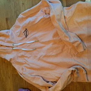 Rosa hoodie  - Säljer en rosa hoodie med trycket 'Yosemite' på bröstet. Den har en justerbar huva med vita snören och ribbade muddar vid ärmslut och nederkant. Perfekt för en avslappnad stil.