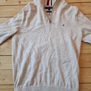 Beige tröja från Tommy Hilfiger - Säljer en stilren beige tröja från Tommy Hilfiger i premium bomull. Tröjan har en dragkedja vid halsen och ett diskret logotypbroderi på bröstet. Perfekt för en avslappnad men snygg look.