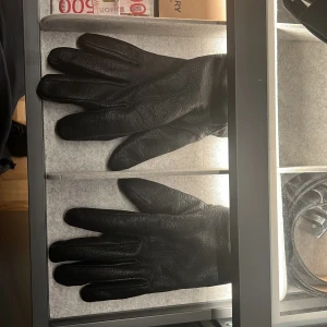 Svarta skinnhandskar - Säljer ett par eleganta svarta skinnhandskar med mjukt foder. Perfekta för kalla dagar och ger en stilren look. Handskarna har en klassisk design och är tillverkade i högkvalitativt material.