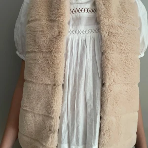 Beige pälsväst från Zara - Säljer en supermjuk beige pälsväst från Zara. Perfekt för att hålla sig varm och stilren under kyligare dagar. Västen är i storlek 140 och passar barn i åldern 9-10 år. Ett måste för garderoben! Västen går att knäppa igen på framsida.