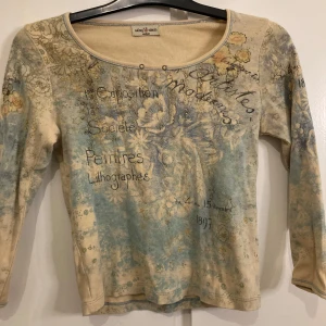 Beige och blå tröja från Skinny Minnie - Säljer en unik beige och blå tröja från Skinny Minnie med ett konstnärligt tryck och blommönster. Tröjan har trekvartsärmar och rund halsringning. Perfekt för dig som gillar en bohemisk stil. 🌼