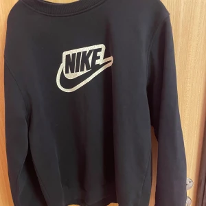 Svart tröja från Nike - Säljer en svart tröja från Nike med deras ikoniska logga i vitt på framsidan. Tröjan har långa ärmar och en rund halsringning. Perfekt för en sportig och avslappnad stil.