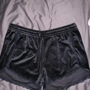 Svarta sammetsshorts - Snygga svarta shorts i mjuk sammet. De har en elastisk midja med dragsko och fina spetsdetaljer längs kanterna. Perfekta för en avslappnad och stilren look.